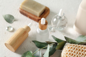Fototapeta na wymiar Bottles of cosmetic products, soap and branch on light background, closeup