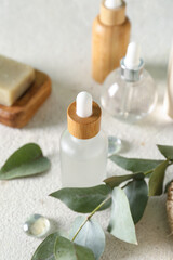 Bottles of cosmetic products, soap and branch on light background, closeup