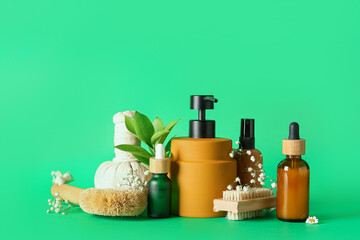 Bottles of cosmetic products, brushes, herbal bag and gypsophila flowers on green background