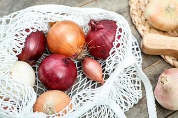 String bag with different kinds of onion on brown wooden background