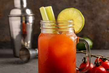 Mason jar of bloody mary with celery and shaker on grey table