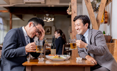居酒屋で酒・ビールを飲みながら同僚・友達と楽しく会話するビジネスマン
