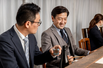 居酒屋・飲み屋のカウンターで部下と楽しくお酒を飲むビジネスマンの男性
