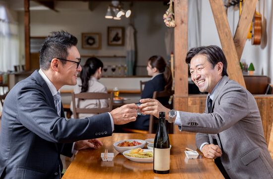 居酒屋で同僚・友達と飲み会・日本酒で乾杯をするスーツ姿のビジネスマン・サラリーマンの男性
