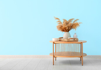 Wooden coffee table with wicker tray, pampas grass in vase and cups near blue wall