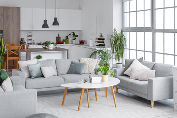 Interior of light open space kitchen with cozy grey sofas and coffee table