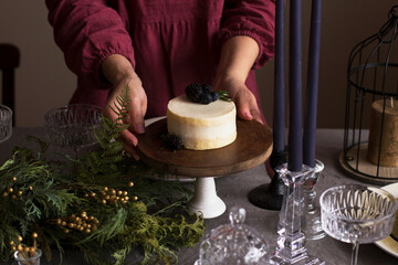 A woman in a burgundy dress sets a festive table for Christmas. Delicious bento cake with berries