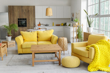 Interior of light open space kitchen with yellow sofa, armchair and wooden coffee table