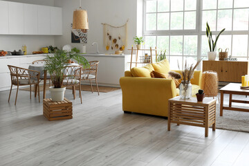 Interior of light open space kitchen with yellow sofa and houseplant on wooden box