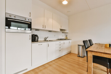 a kitchen and dining area in a house with white cabinets, wood flooring and an oven on the wall