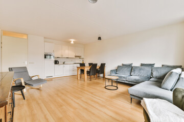 a living room with wood flooring and white walls on the walls is an open kitchen area in the background