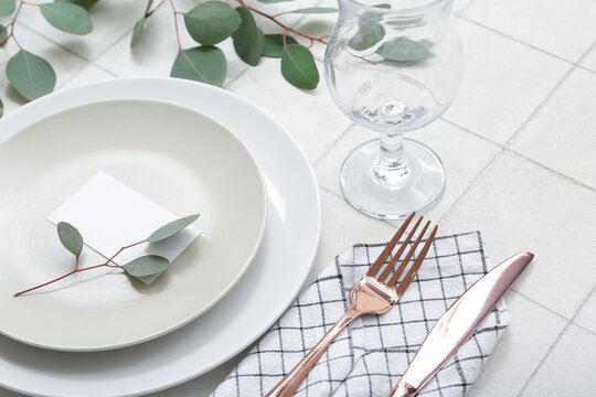 Beautiful table setting with blank invitation card and eucalyptus branches on white tiled table