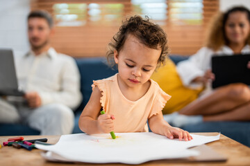 African kid painting on paper with parents behind indoor in house. 