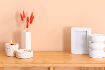Fototapeta na wymiar Holders with burning candles and blank frame on table near beige wall in room