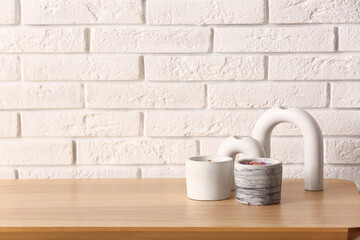 Holders with candles and decor on table near light brick wall in room