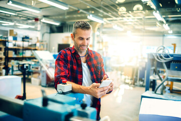 Mid adult man using his smart phone while working in a printing press office