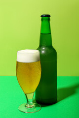 Bottle and glass of cold beer on green background