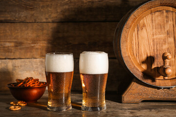 Glasses of cold beer with pretzels and barrel on wooden background