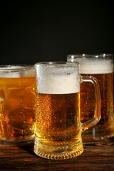 Mugs of cold beer on wooden table, closeup