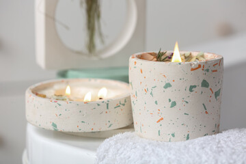 Holders with burning candles and towel on bathtub in bathroom, closeup