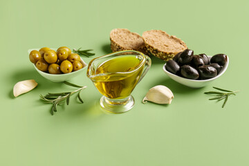 Bowls with ripe olives and gravy boat of oil on green background