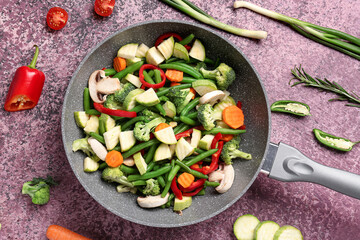 Frying pan with fresh vegetables on purple background