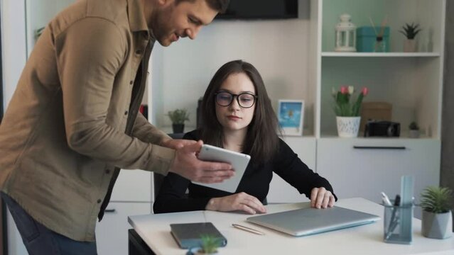 The employee comes to his young boss in her office and shows the completed work on a tablet, the female boss evaluates the work positively.