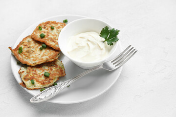 Plate of tasty zucchini fritters with sour cream on light background