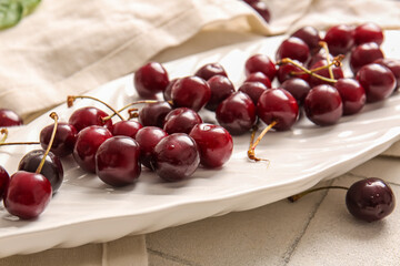 Plate with sweet cherries on white tile background