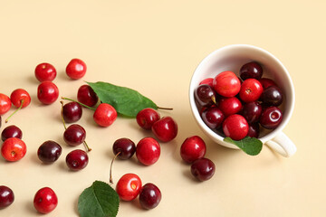 Cup with sweet cherries and leaves on beige background