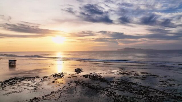 Drone clip of beautiful reflection of golden sunset on calm lagoon and open ocean waves at G-land, Java, Indonesia. Observation tower on reef following international surf competition.