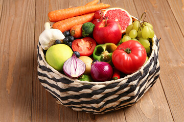 Wicker bowl with different fresh fruits and vegetables on wooden background