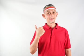 Portrait of Asian Man wearing red and white Indonesia flag attribute looks happy doing positive gesture with thumbs up, smiling
