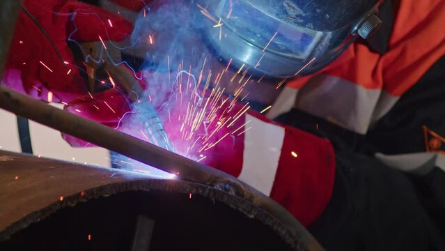 Marvel at the precision and skill of a welder as flashes of light and sparks illuminate the work area, showcasing the craftsmanship involved in industrial metal welding.