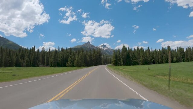 Riding a car on asphalt mountain road in Wyoming. Sunny summer day with blue sky and white clouds
