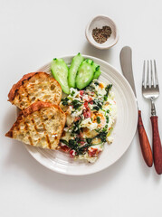 Baked eggs with mozzarella, spinach and grilled rustic bread on a light background, top view