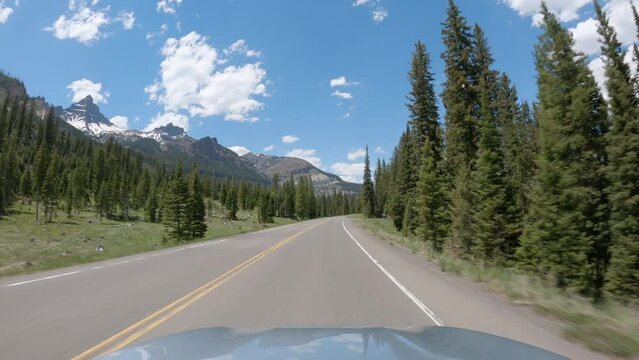 POV Driving a car on asphalt road in Wyoming mountains towards Yellowstone National Park. Blue sky on sunny day