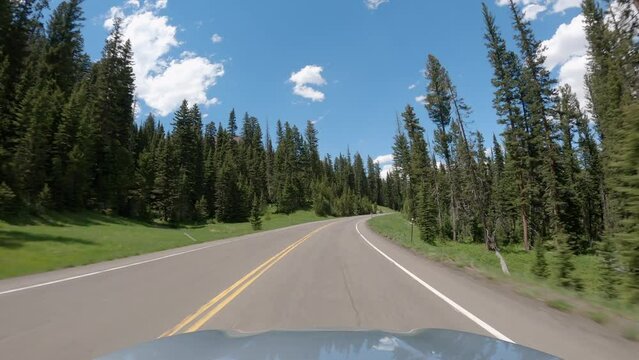 POV Driving a car up on asphalt road in Wyoming mountains towards Yellowstone National Park. Blue sky on sunny day
