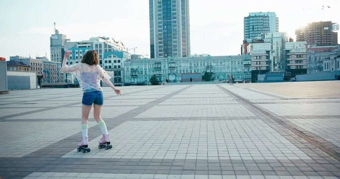 Young fit woman on roller skates riding outdoors on urban street. Smiling girl with rollerblading on sunny day