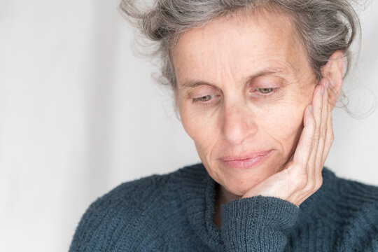 Close up head and shoulders view of older woman in blue sweater looking rueful with head in hand (selective focus)