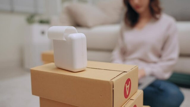 Young asian woman selling online receiving order via laptop and using label printer to printing customer address attach to the parcel box. Business Online and delivery shop concept