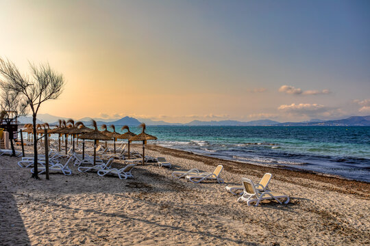 Can Picafort Beach with straw umbrellas and sun loungers, morning with no people, against the turquoise sea. Can Picafort, Balearic Islands Mallorca Spain. Travel agency vacation concept.