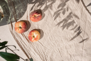 Aesthetic lifestyle fruit pattern with peaches, crumpled linen fabric and floral sunlight shadow on beige table background