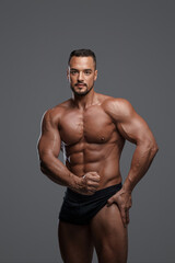 Fototapeta na wymiar Stunningly handsome male model with a sculpted physique poses in black briefs against a grey backdrop, radiating sexiness and allure