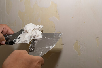 The builder's hands use a spatula to apply plaster to the wall.
