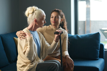 Pretty multiethnic girl in casualwear looking at her grandmother while embracing her by shoulder...