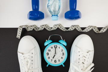 Top view photo of white alarm clock dumbbell sneakers and other sports equipment.