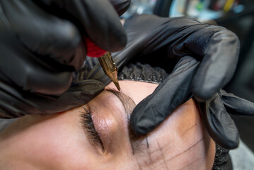 The cosmetologist makes a permanent makeup of the eyebrows - obrazy, fototapety, plakaty