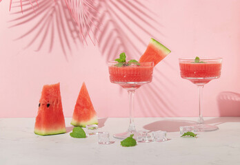 Summer creative layout with cocktail glasses and watermelon slices with pink palm leaf on pastel pink background. 80s or 90s retro aesthetic idea. Minimal summer drink idea.