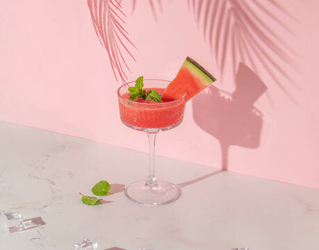 Summer creative layout with cocktail glass and watermelon slice with pink palm leaf on pastel pink background. 80s or 90s retro aesthetic idea. Minimal summer drink idea.
